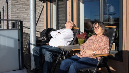 Bildet viser to personer som nyter solen på balkongen sin i boligprosjektet Skårerløkka på Lørenskog, rett utenfor Oslo.