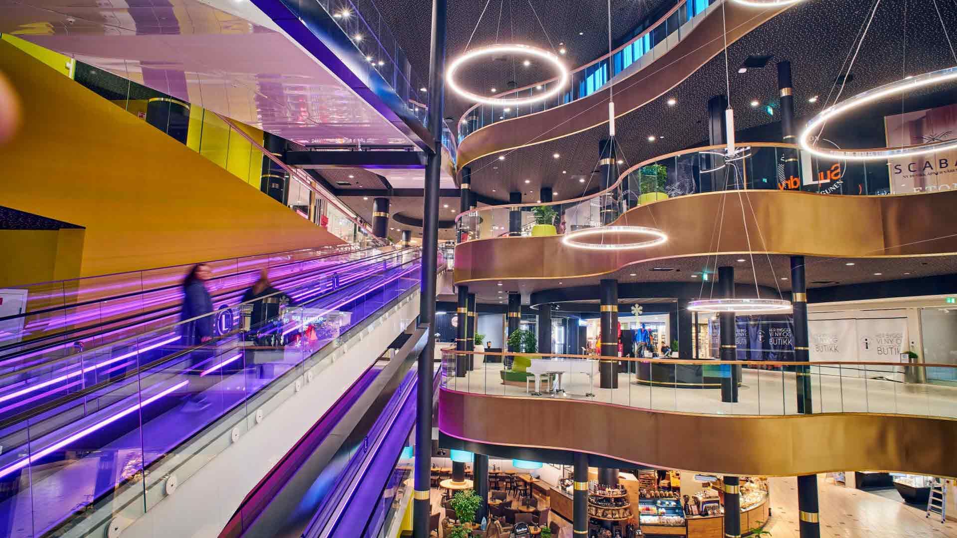 Interiør av kjøpesenter med flere etasjer og rulletrapp i spreke farger. Foto til artikkel om Lagunen Storsenter som tok omsetningsrekord i 2022.